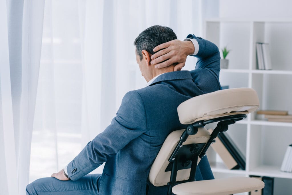 adult businessman with painful backache sitting in massage chair at office waiting for a tulsa chair massage